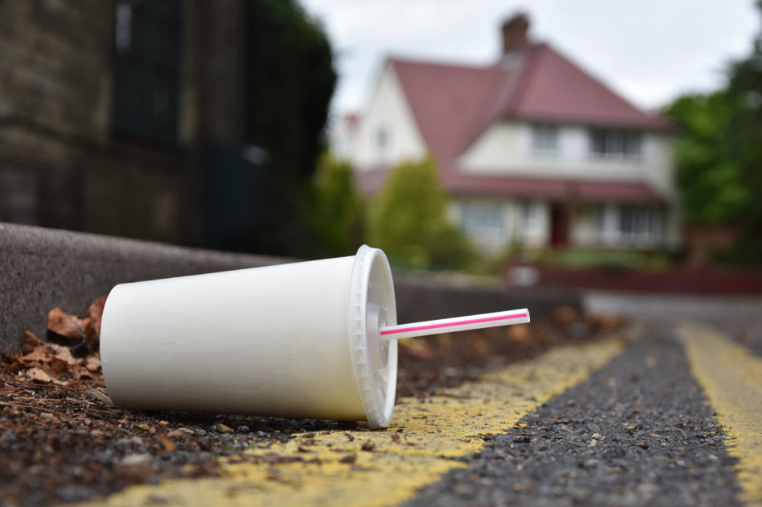 Photo of disposable paper cup on its side at the edge of a road.